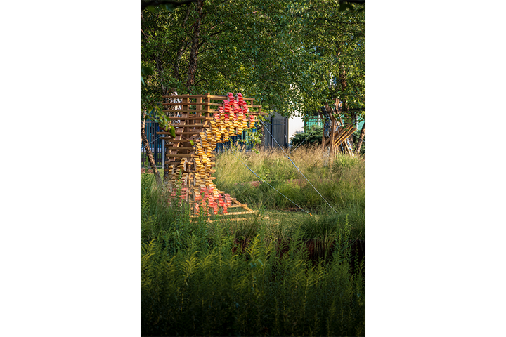 Wood and ceramic sculpture outdoors next to tree and native grasses