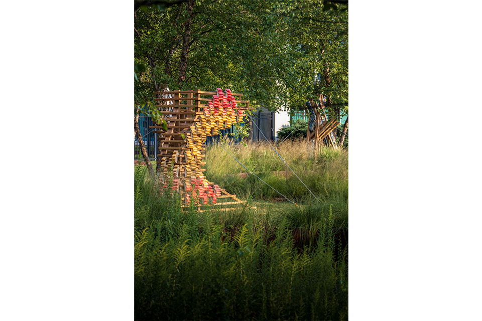 Wood and ceramic sculpture outdoors next to tree and native grasses