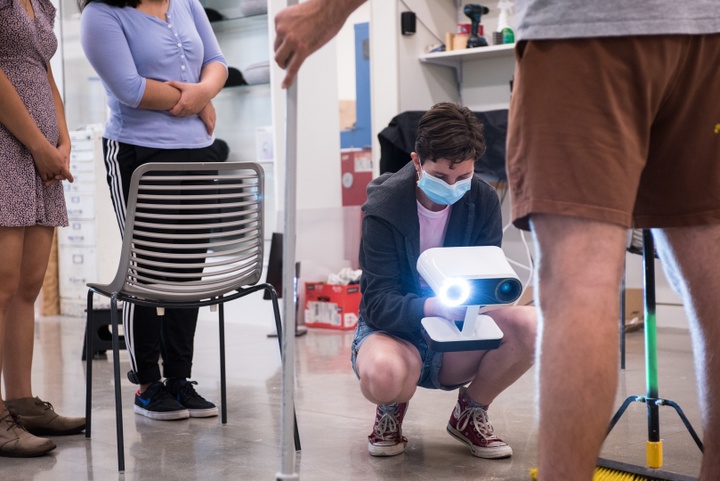 Person with handheld scanning device crouches to scan someone's feet.