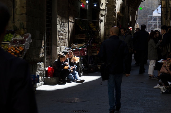 Three friends eating sandwiches on a stoop in the sunlight. The rest of the narrow street is in shadow.