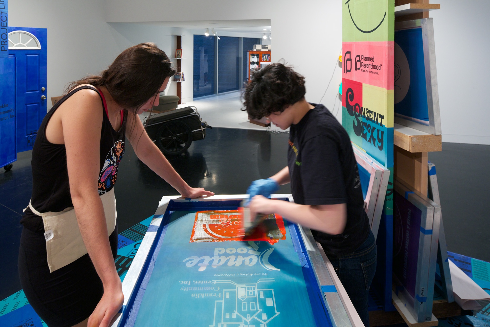 Two light-skinned, young people work on a screenprint in a gallery space.