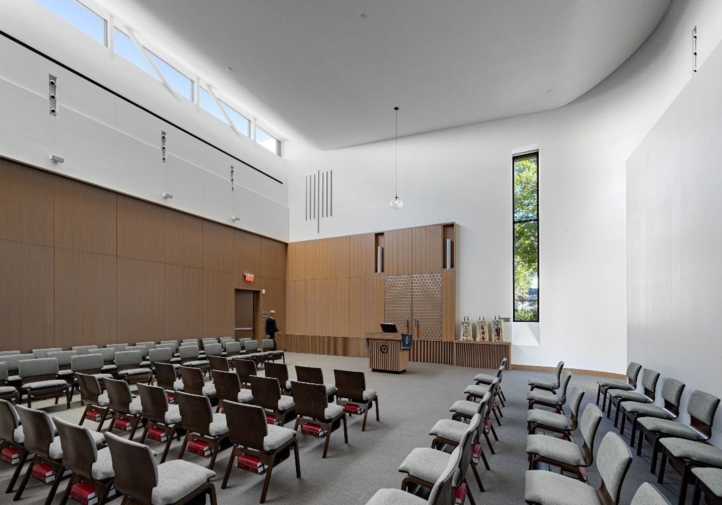 Gemini said An interior shot of a contemporary, brightly lit synagogue sanctuary with high white ceilings and a curved wall. The space features clean architectural lines and a minimalist aesthetic.