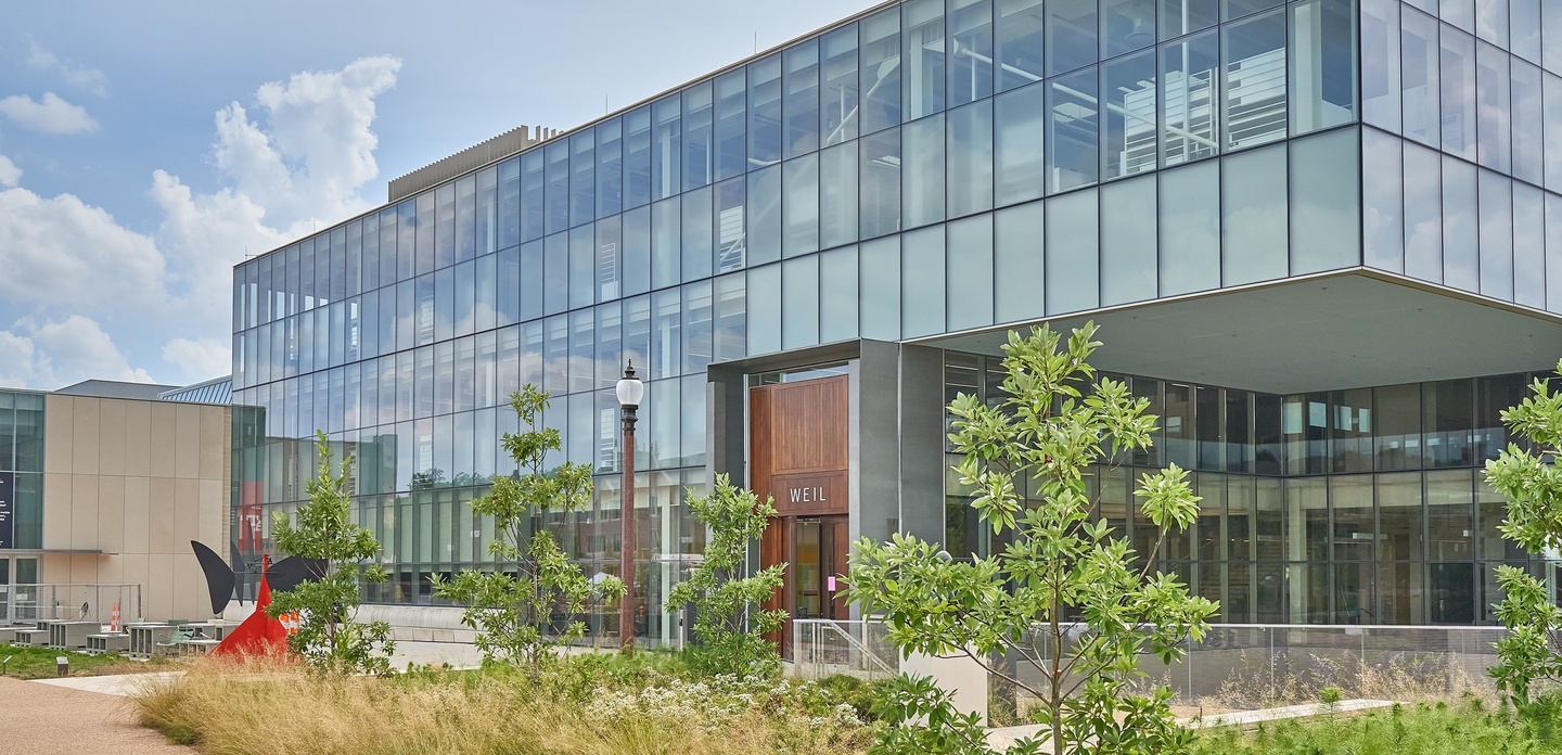 A glass-facade building with three stories. A red Calder sculpture sits on the patio out front.