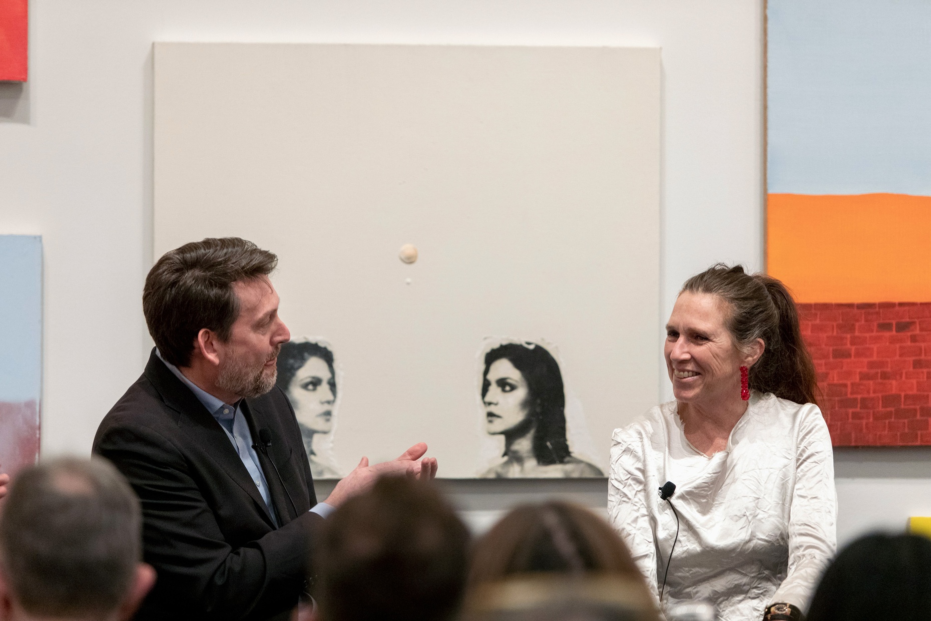 A man speaks with a woman before works of art and in front of a crowd.
