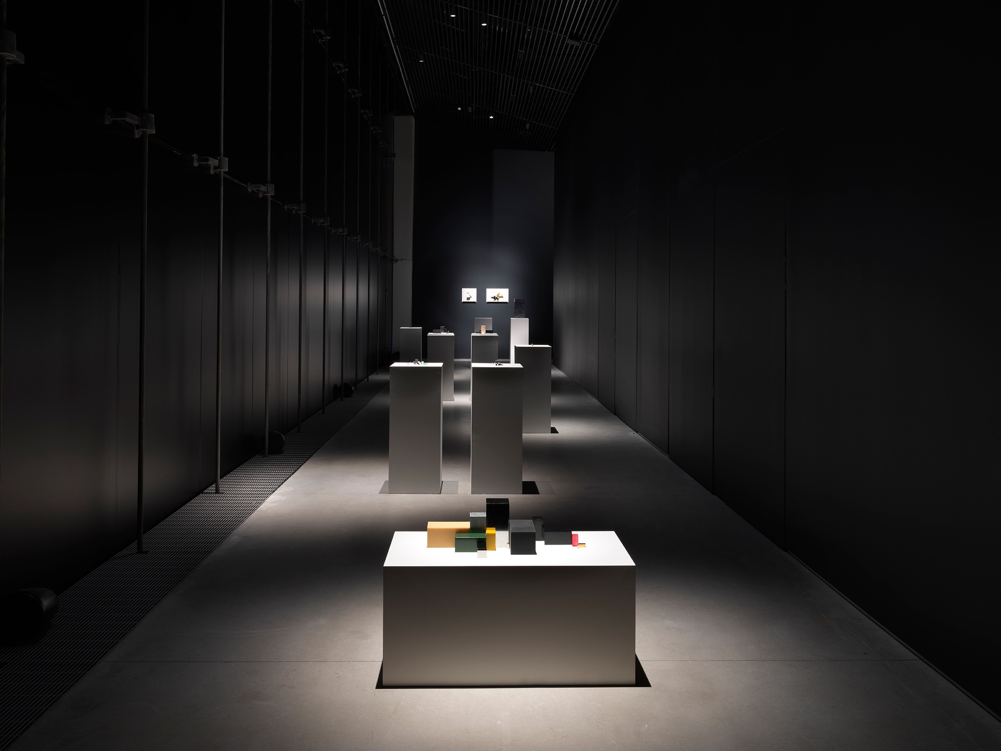 A gallery hallway with a line of plinths topped by sculptures assembled from small rectangular blocks