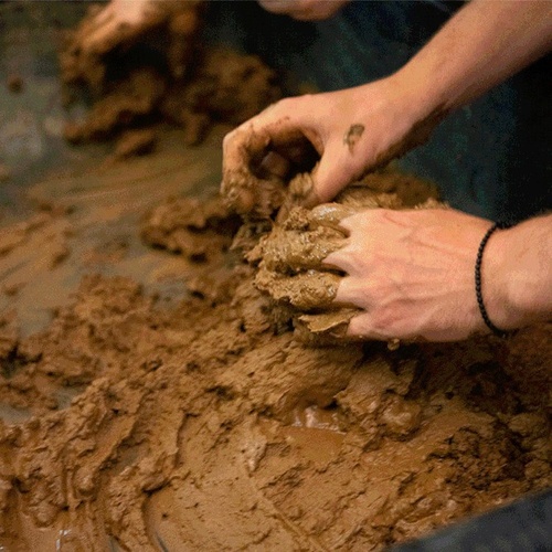 Two hands modeling mud placed on a surface. 
