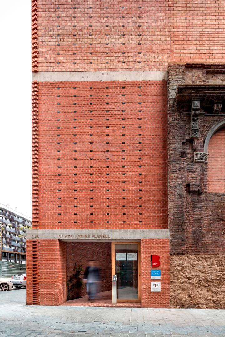 Exterior photo of a multistory red brick building with a pattern of missing bricks and a decorative finish of bricks angled on the corner.