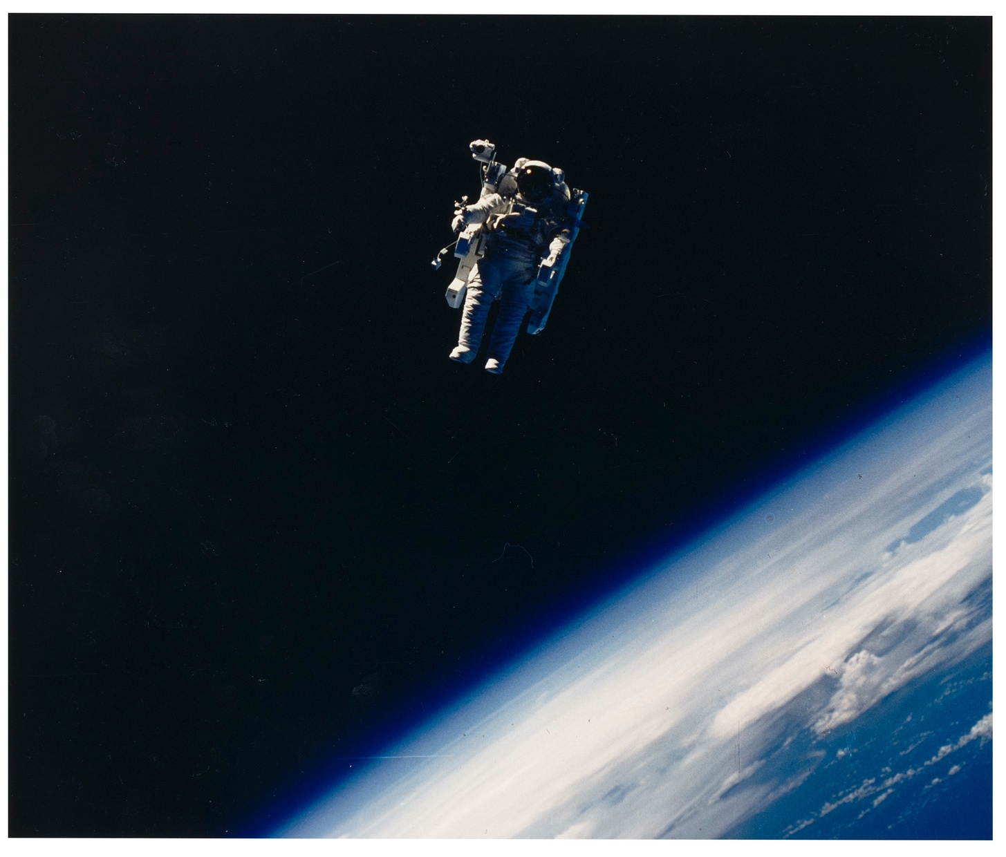An astronaut, wearing a spacesuit and large backpack, floats untethered in space with Earth’s atmosphere below.