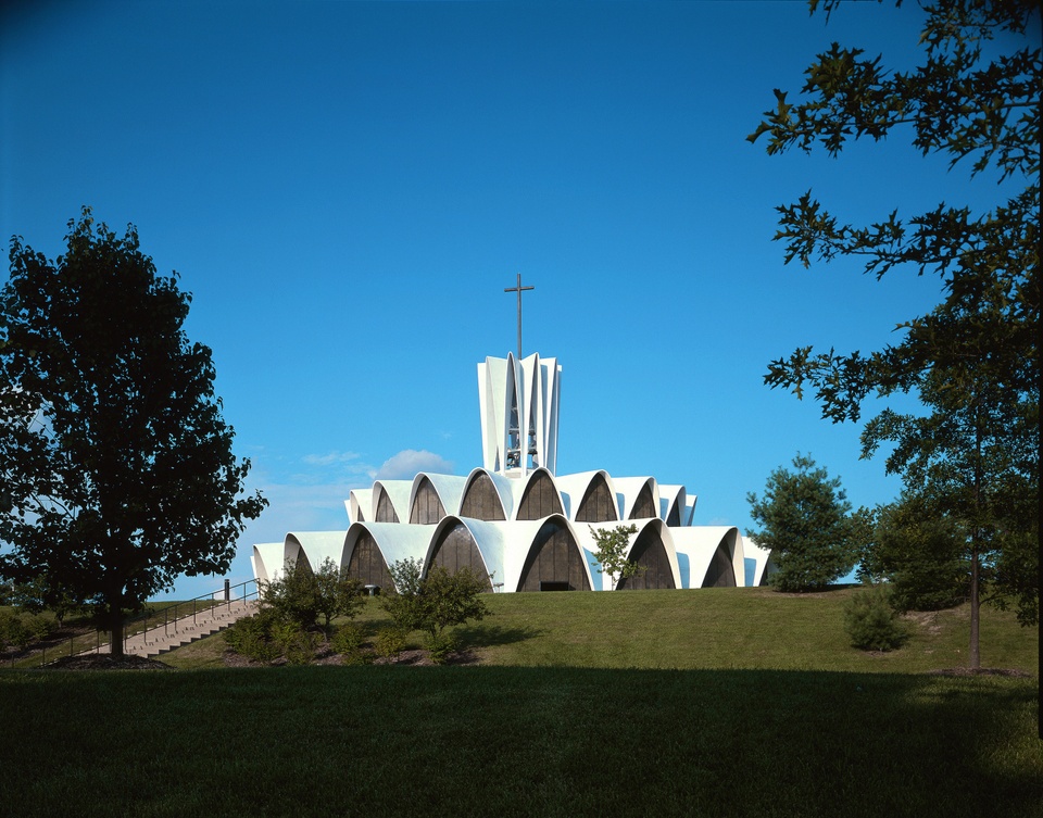 Exterior photo of an abbey with curved architecture, framed by trees.