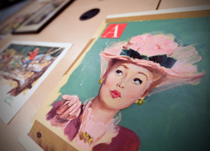 Close-up view of a gouche painting of a woman in a pink frilly hat.