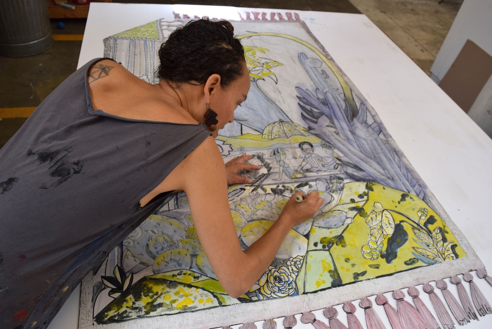 Over the shoulder view of Paula adding details onto a large print on a large table