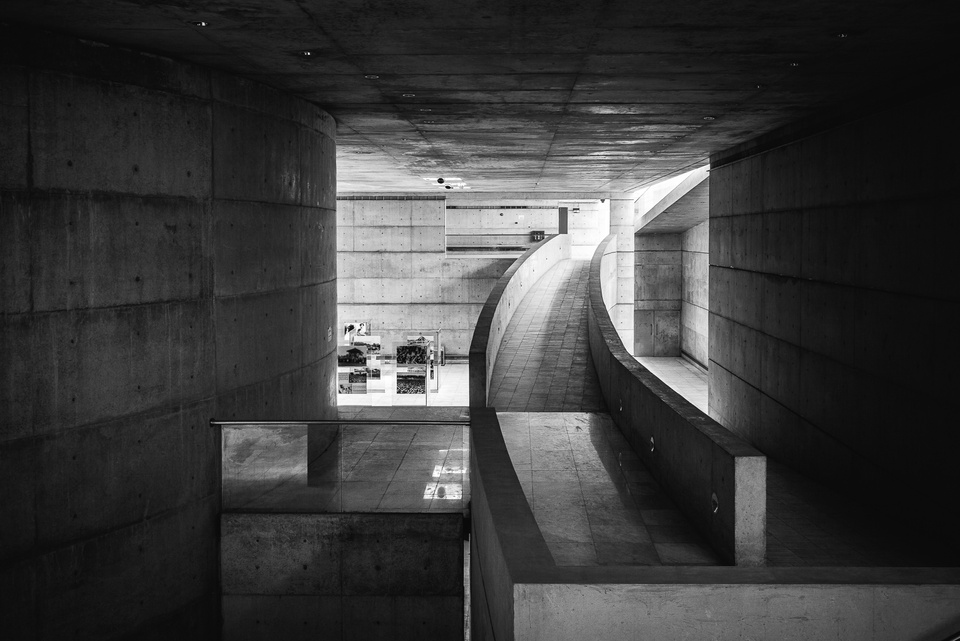 Black-and-white interior photo of a curved walking path to the right of an interior space with work on display.