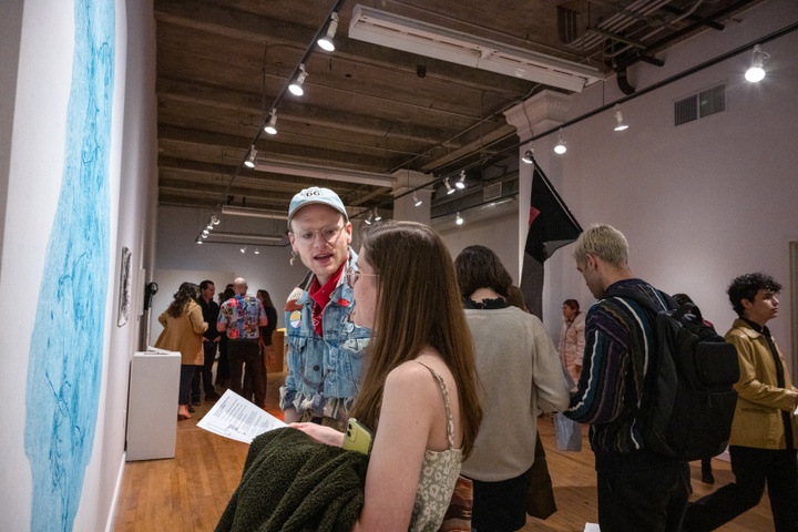 Two people stand in front of a cyan-colored print in a gallery and discuss it.