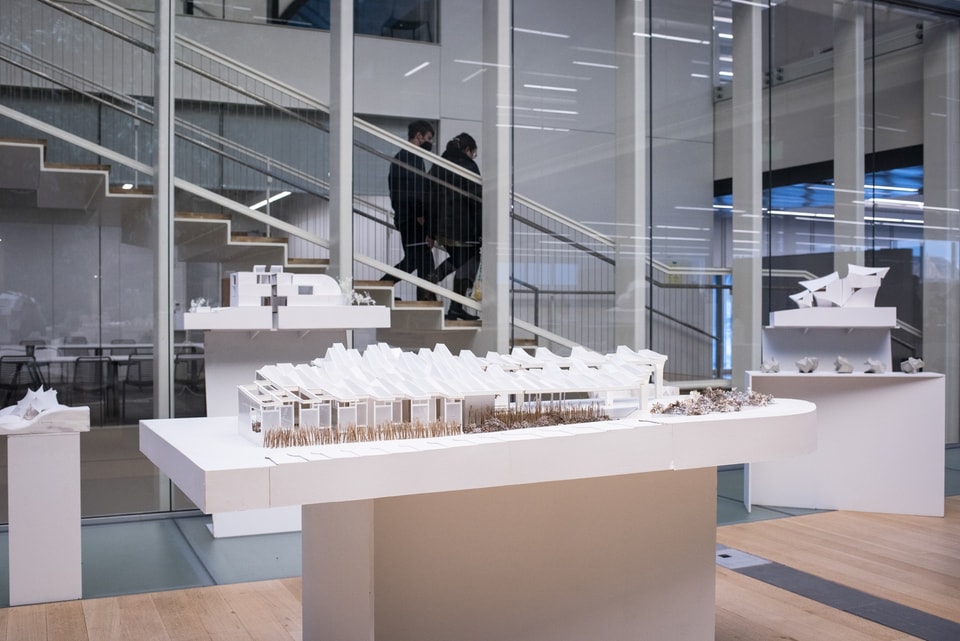 White architectural model of a long, low building on a stand in an interior courtyard.