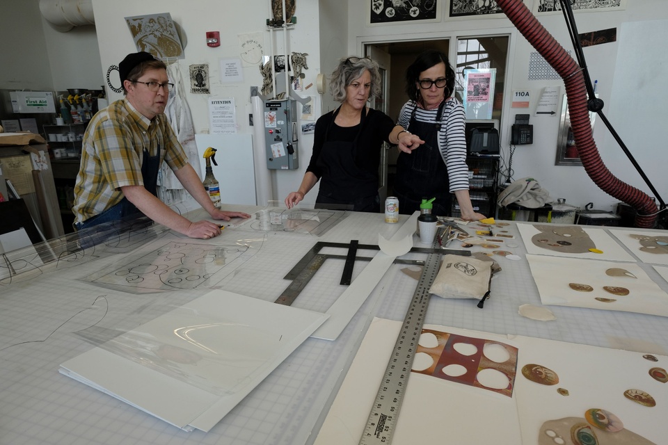 Artist working in the print shop, looking at collage material