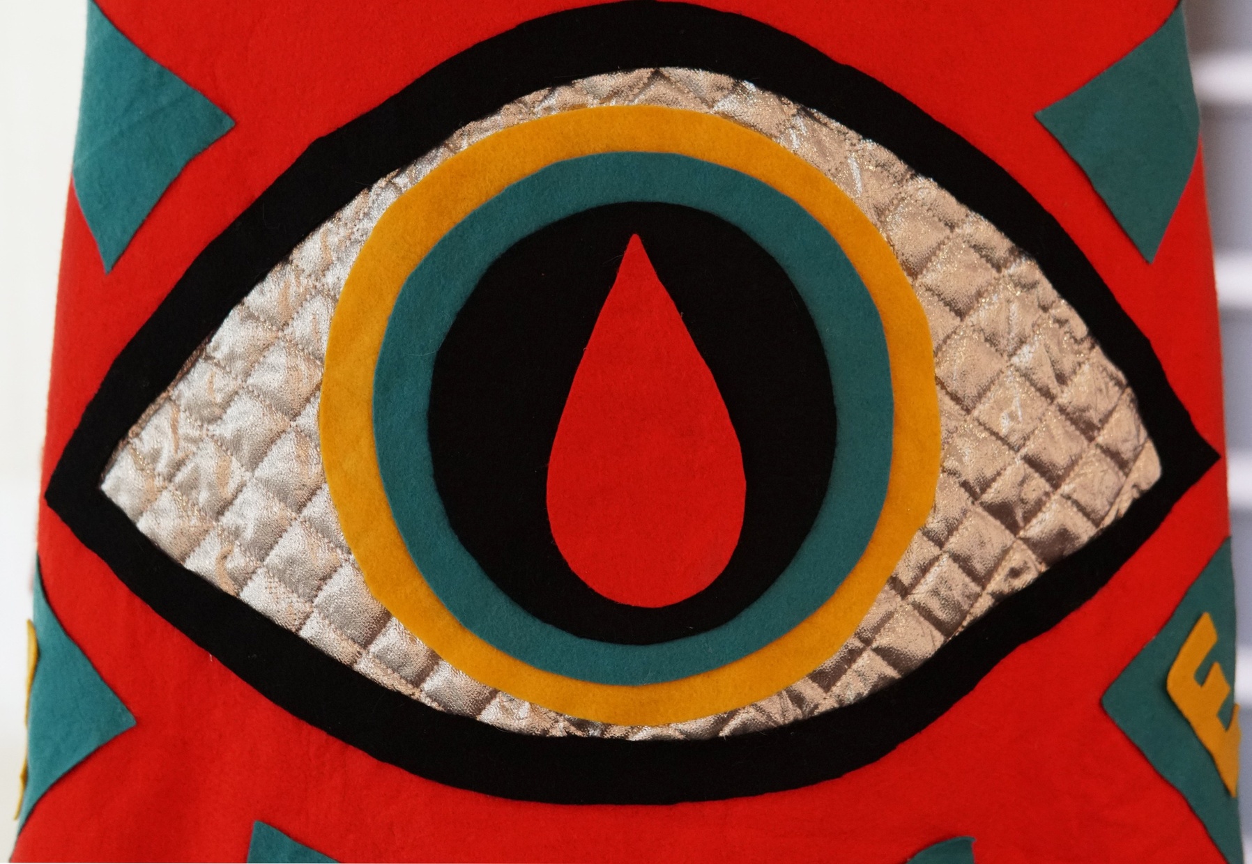 A long, red cape with a large eye, made of red, black, blue, yellow, and silver fabric; blue triangles, bearing yellow letters “L O V E,” radiate from the eye.