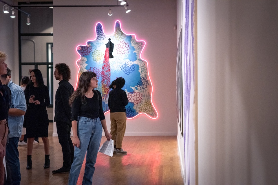 Visitors in front of Jorge Rios' large painting on cowhide outlined with LED neon lights