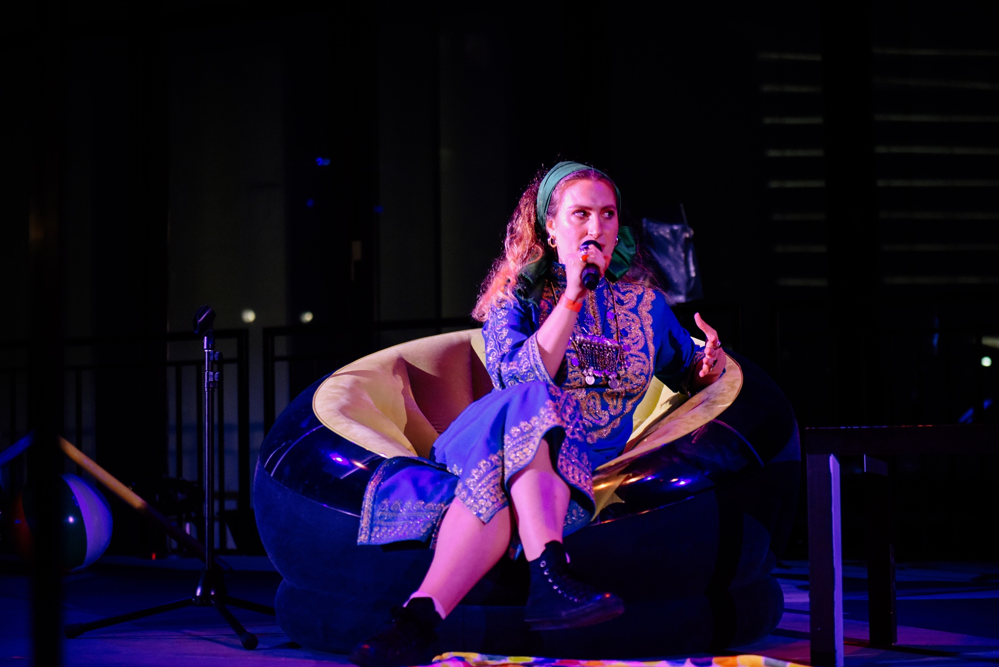 Woman sitting and speaking on dramatically lit stage.