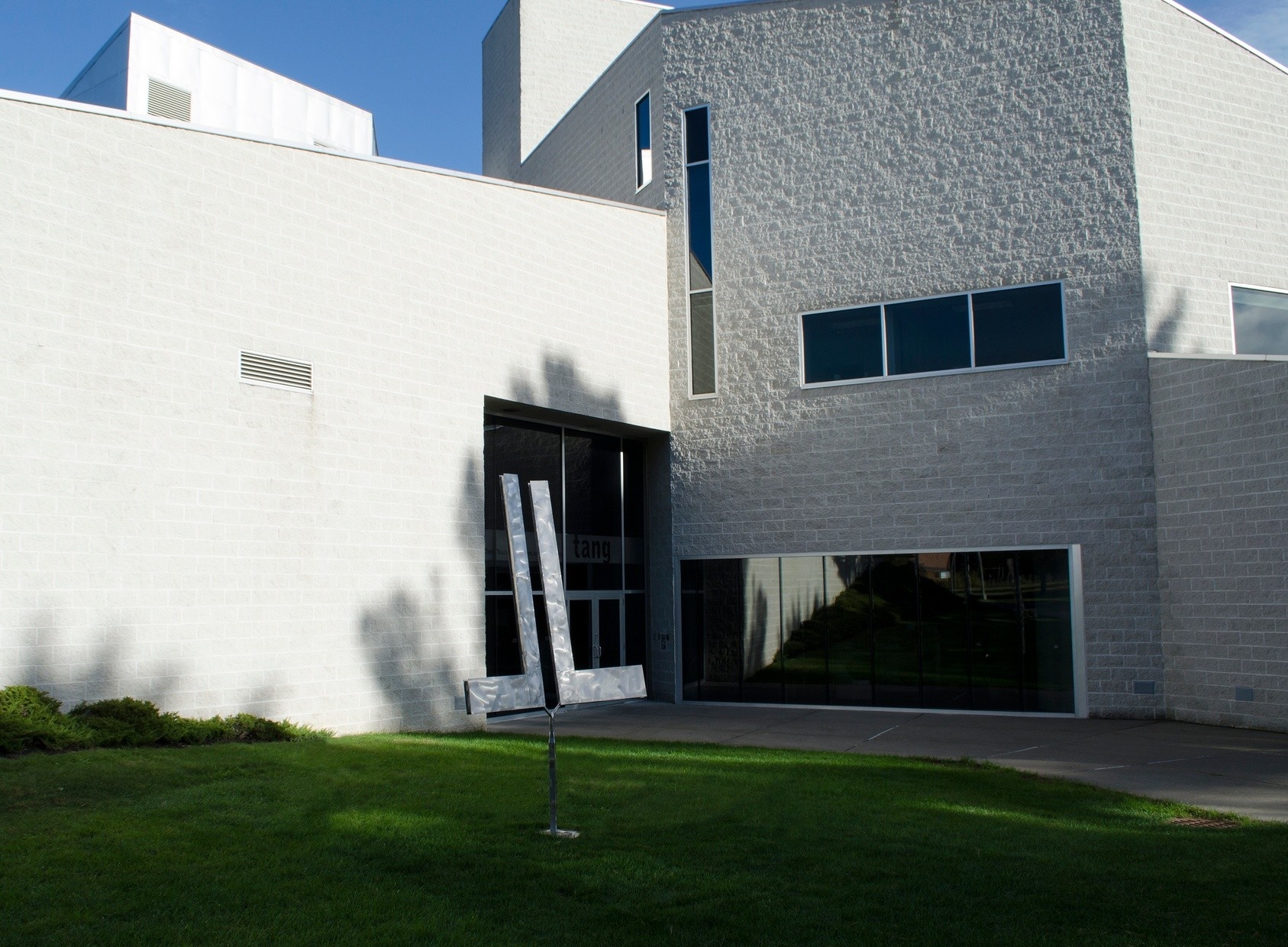 A sculpture sits in the grass outside of a gray brick building.