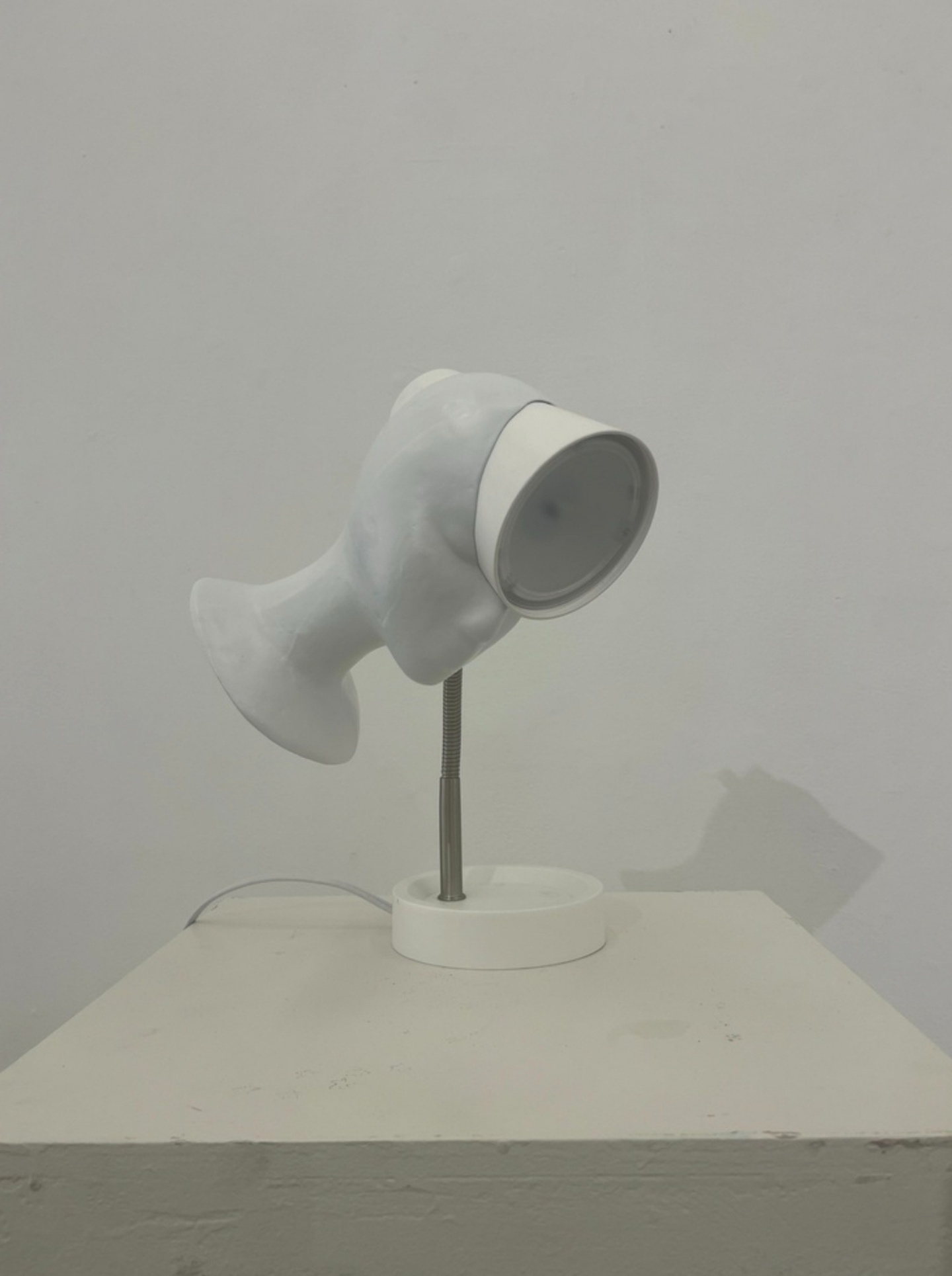 A minimalist, white, clay bust whose head is fazing through a lamp.