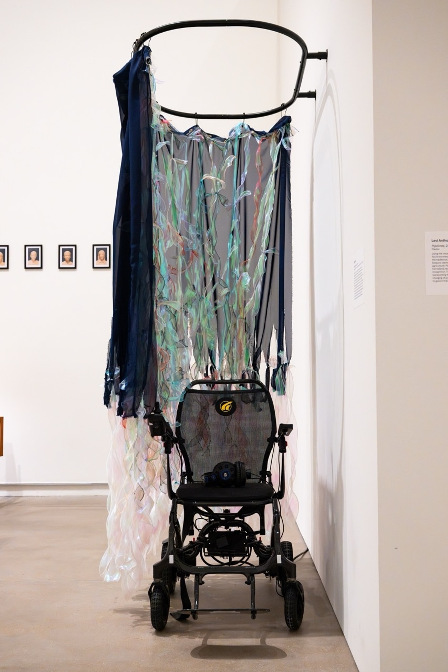 a wheelchair surrounded by a curtain made of chiffon and ribbon in a gallery