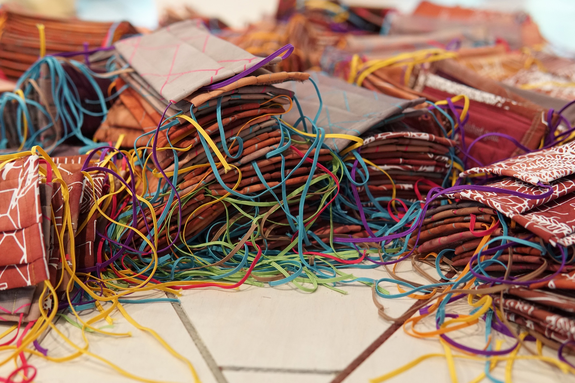 Numerous, colorful, handmade masks piled on a white tiled floor.