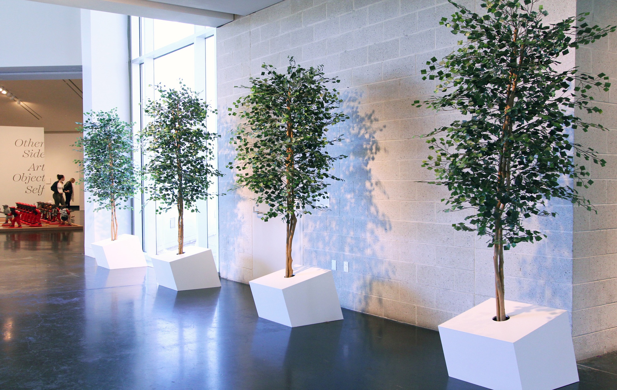 Four trees lined in a row sculpted with wood and paper green squares.