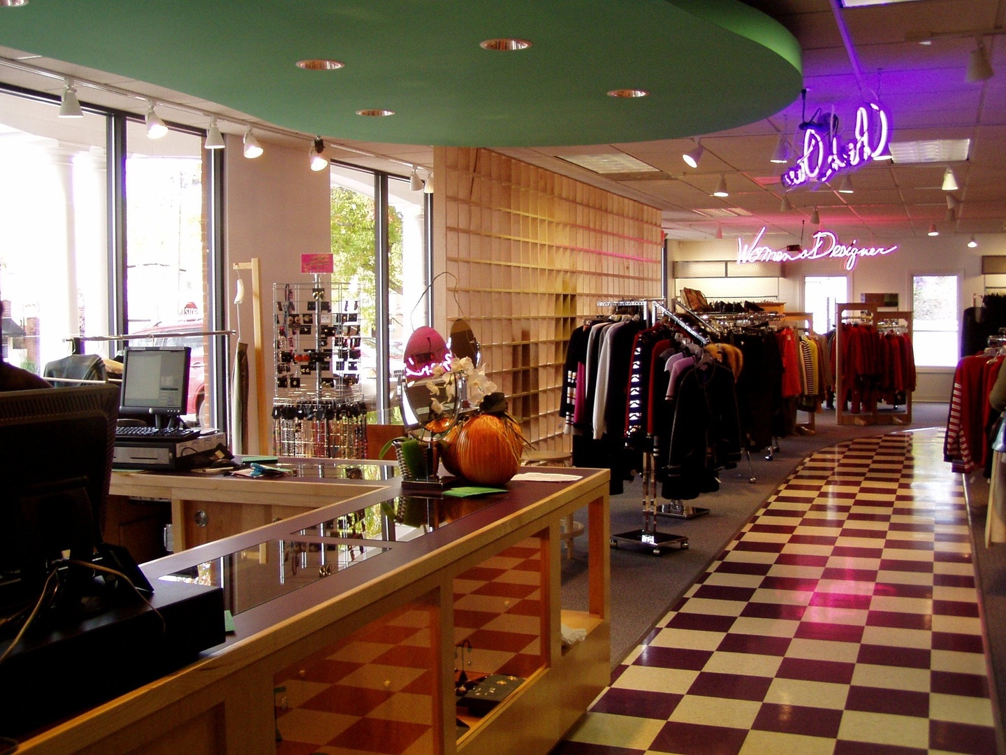 An interior view of the retail shop with a counter and register int eh foreground, checkered flooring, and neon signage descriptive of the clothing for sale