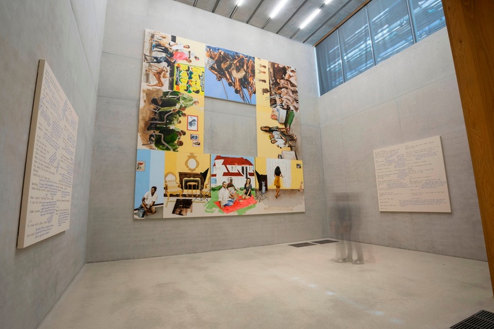 Museum installation featuring a large-scale, 11-panel work, configured as a square with a hole in the middle, featuring various, brightly painted scenes of people. Single artworks with cream-colored backgrounds and text are hung on the walls to the left and right.