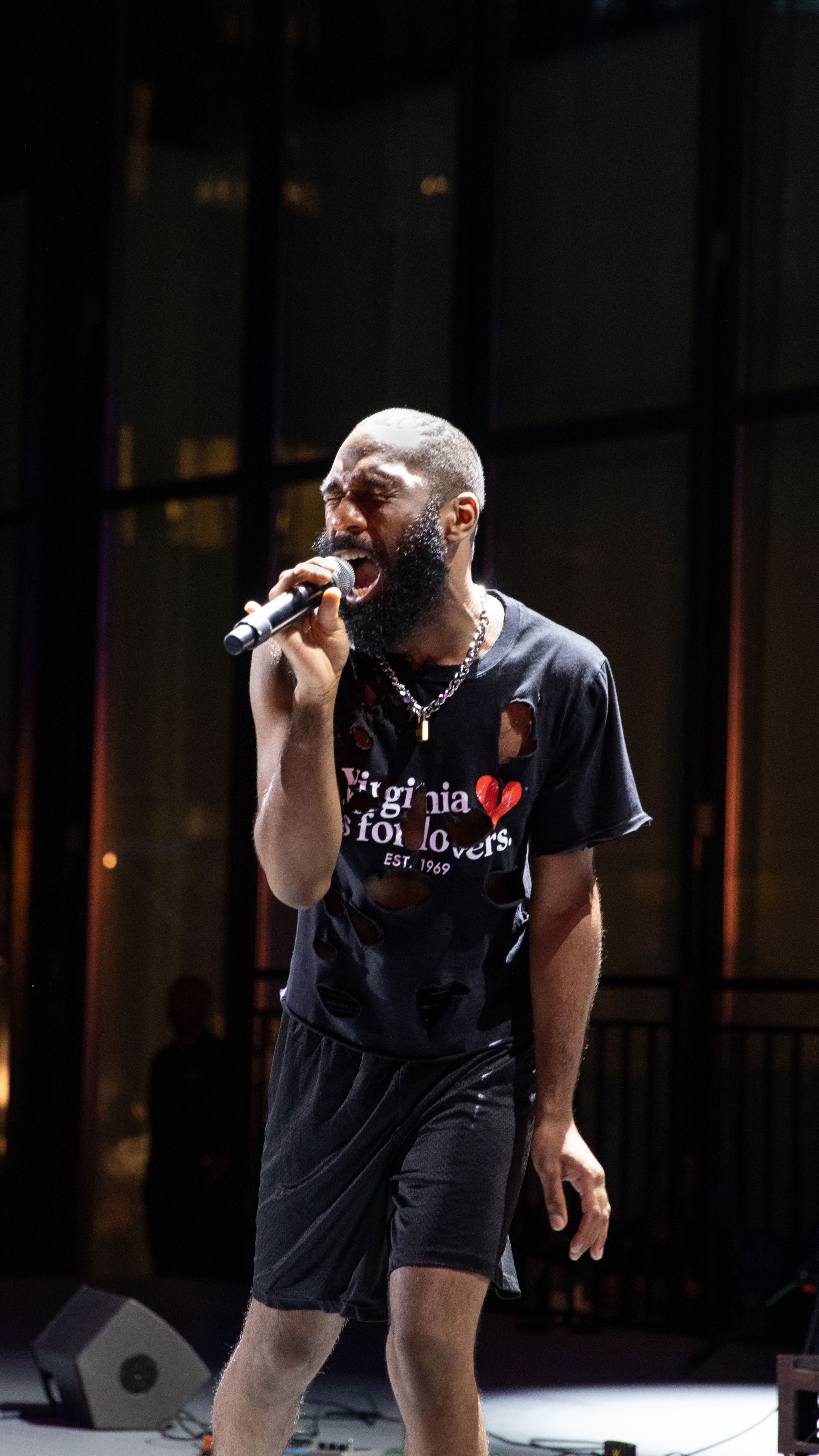 Man singing into mic on dramatically lit stage.