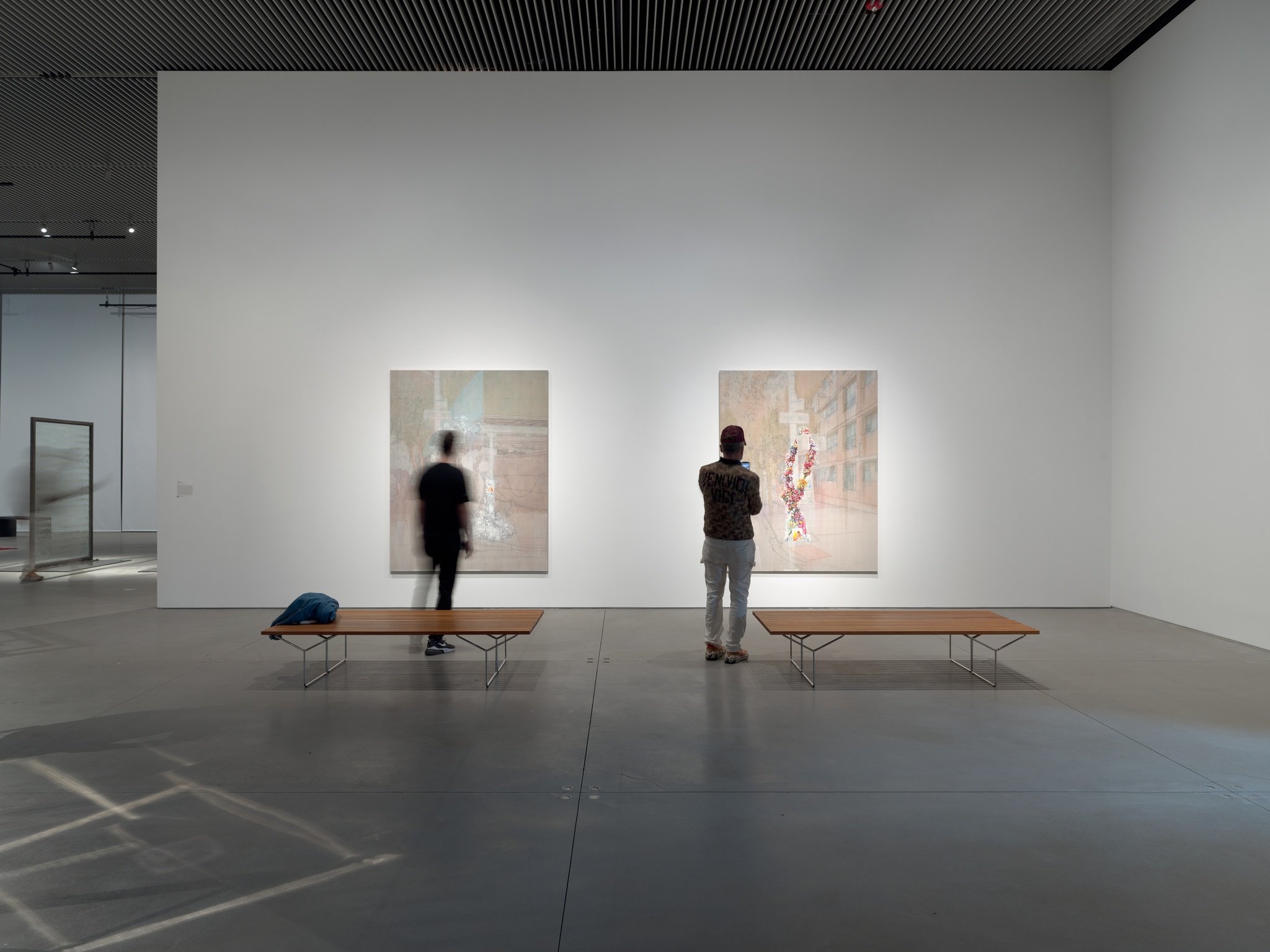 An art gallery with two people standing in front of two large paintings hanging on a white wall