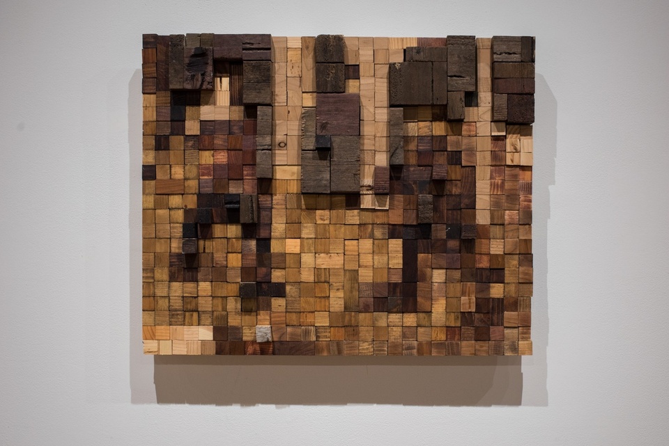 Wooden sculptural wall-art made of small blocks of differently colored wood glued together in a pattern.