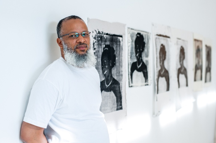 Meleko Mokgosi leaning against a wall next to his black and white artwork