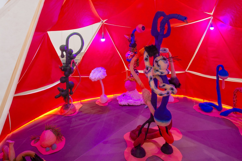 Detail of the bright pink inside of a dome-like tent. There are multiple brightly colored irregularly-shaped standing sculptures resembling intestines