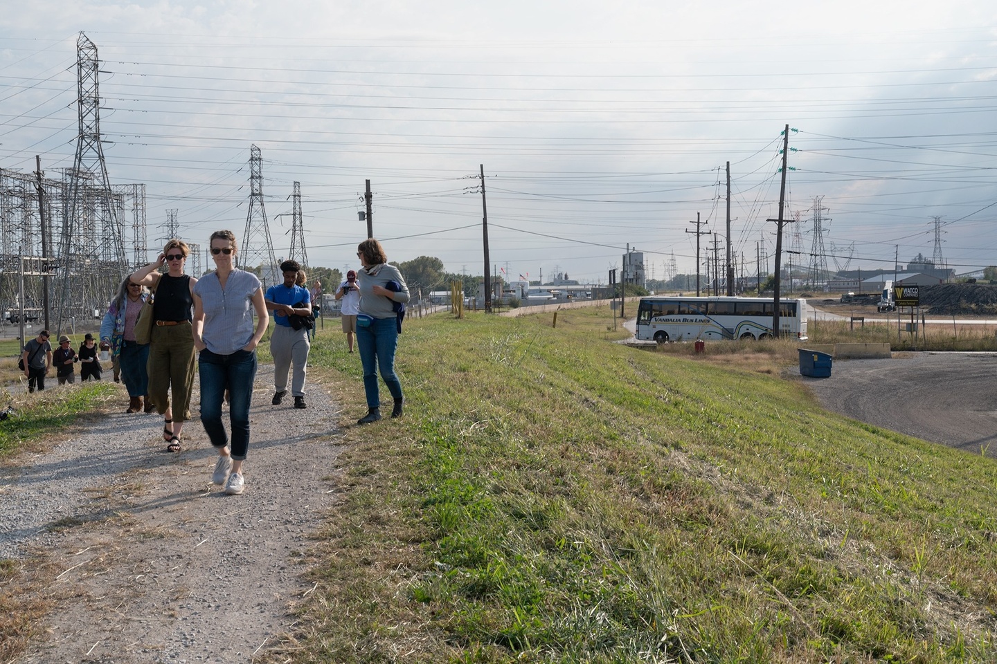 A group of students walks along an unpaved road near an electrical grid hub.