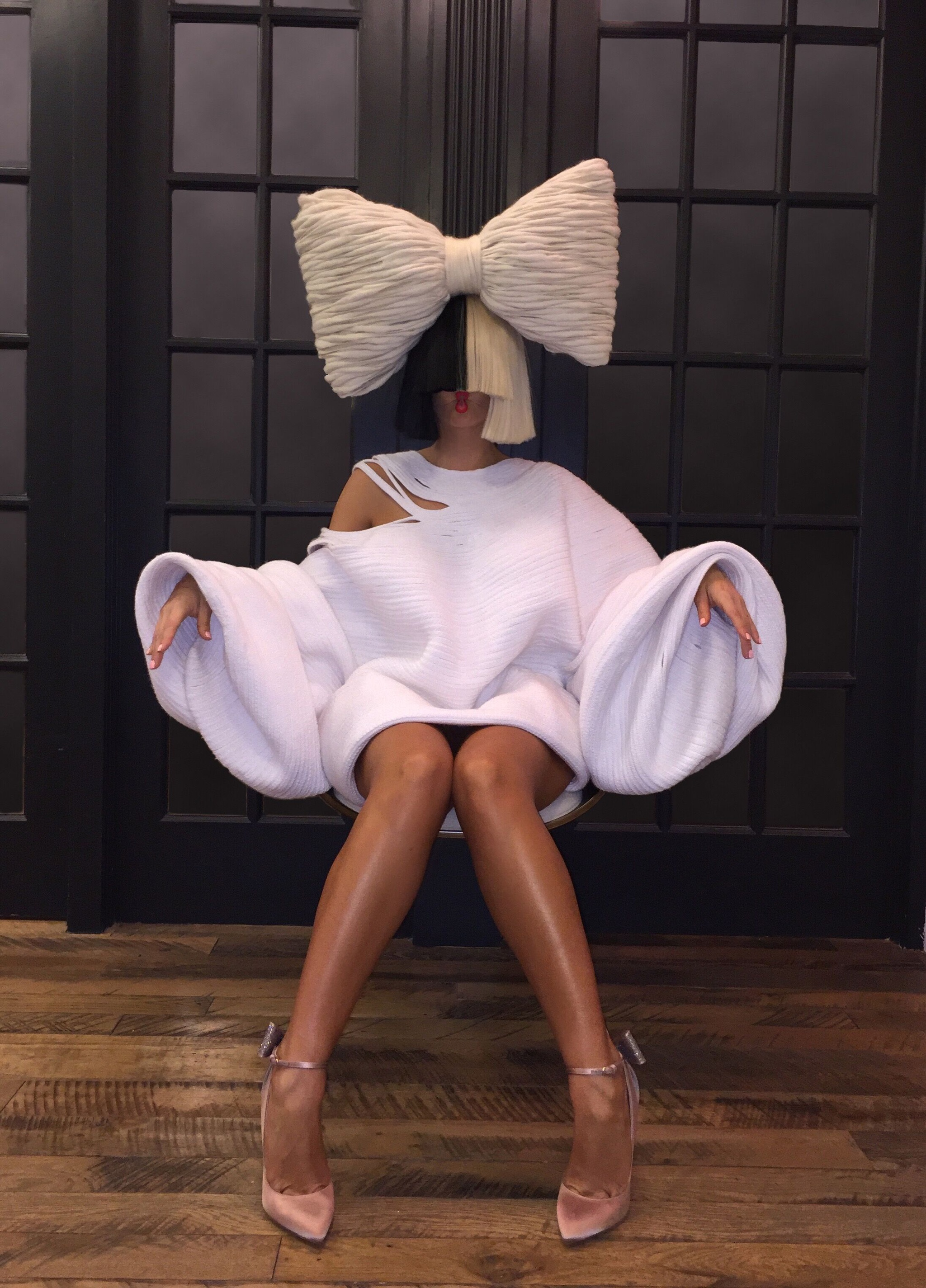 A portrait of Sia sitting in a white dress in a chair