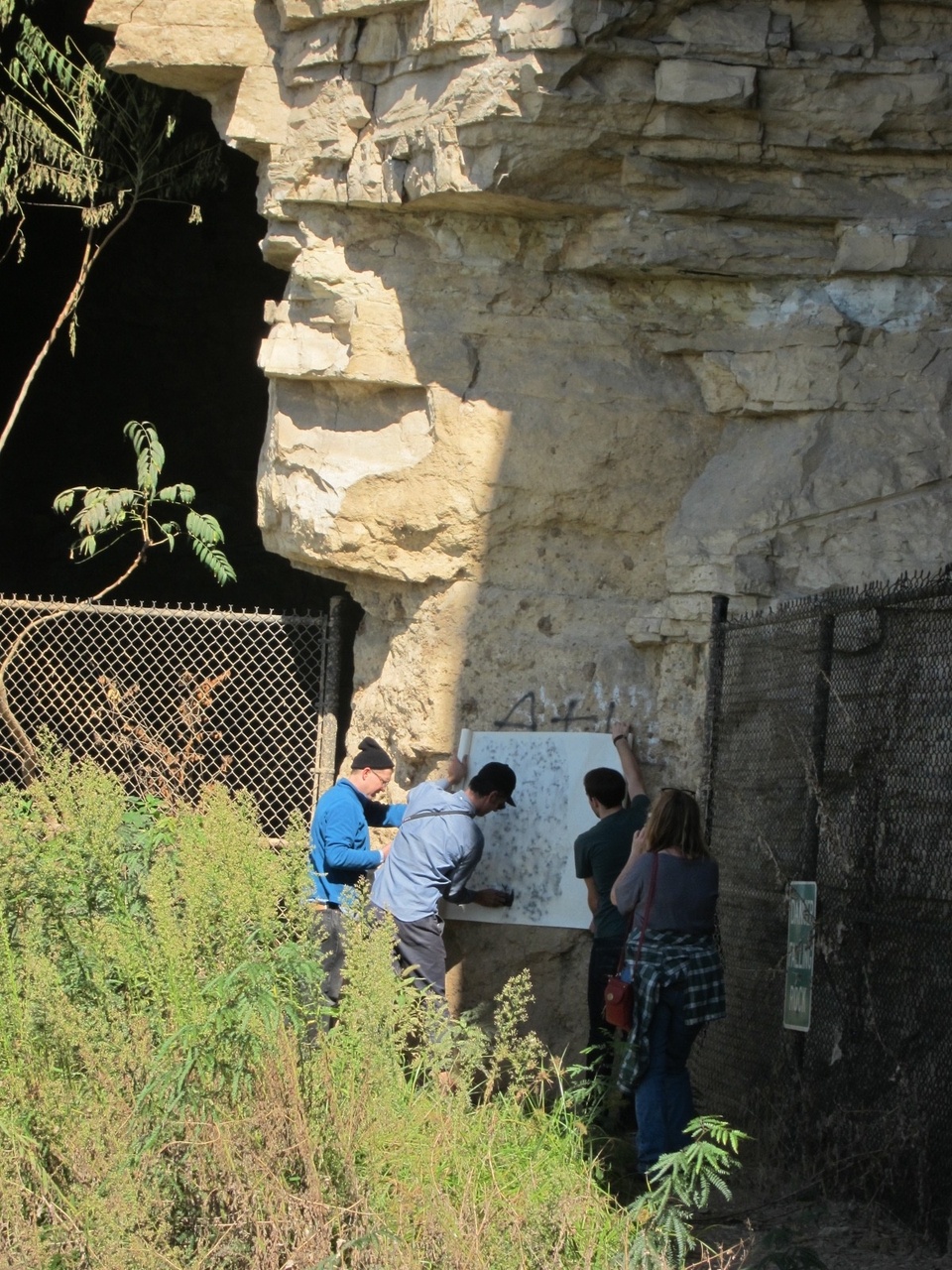 Shaun and two others seen from a distance standing beside a large piece of white paper pressed against a large rock