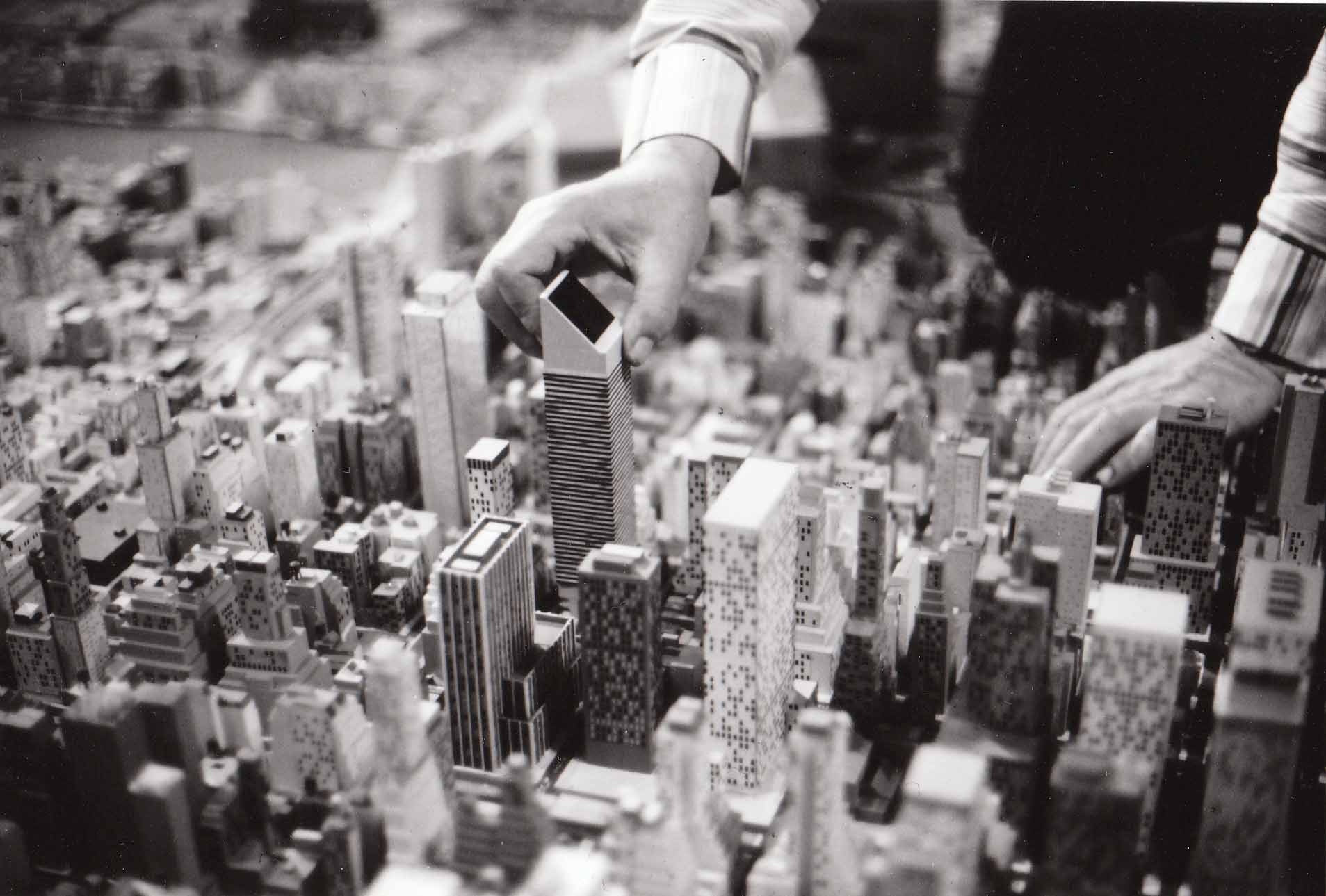 A close up of model buildings on *The Panorama of the City of New York* with two hands entering the frame to adjust the placement of the Citicorp building