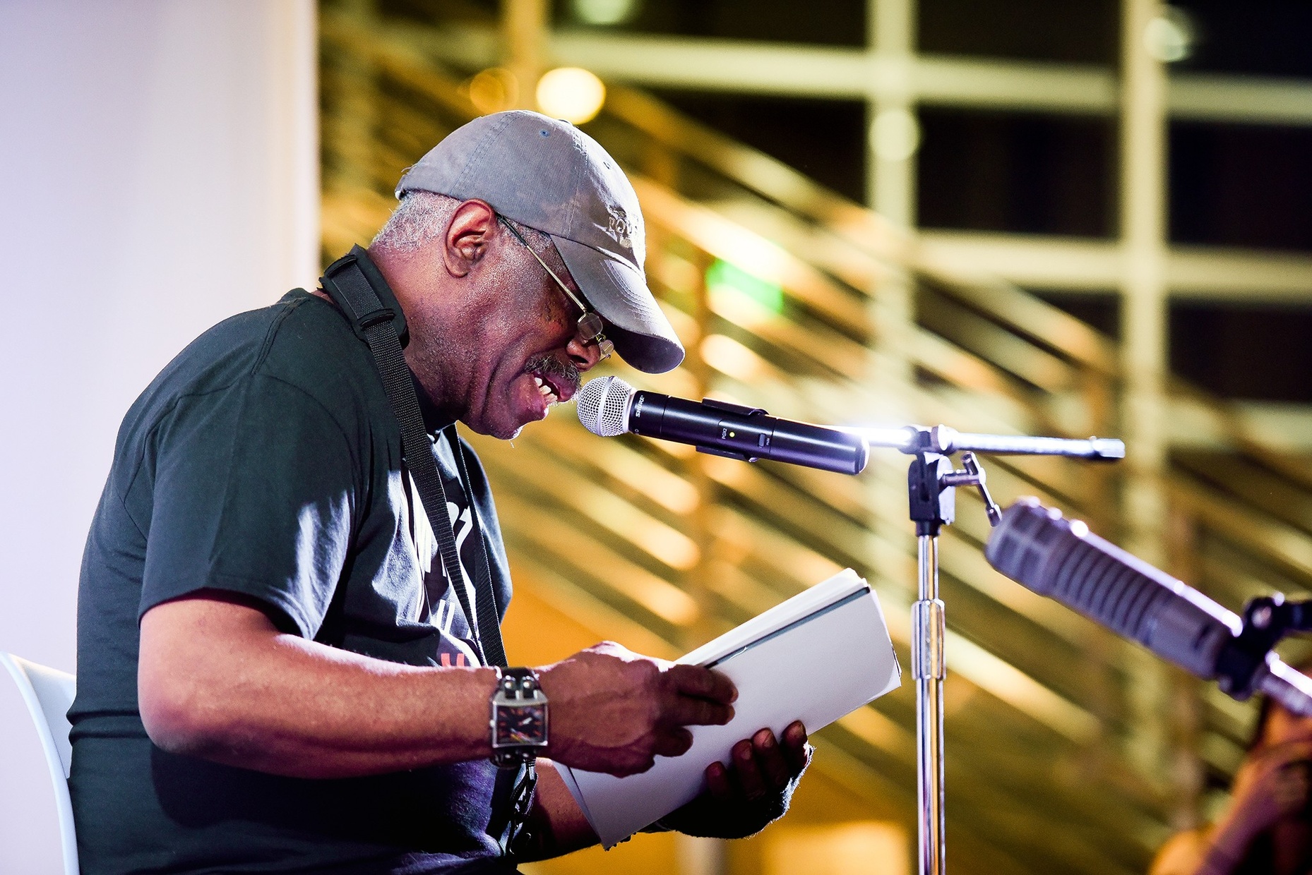Photo of a man reading from a booklet into a microphone.