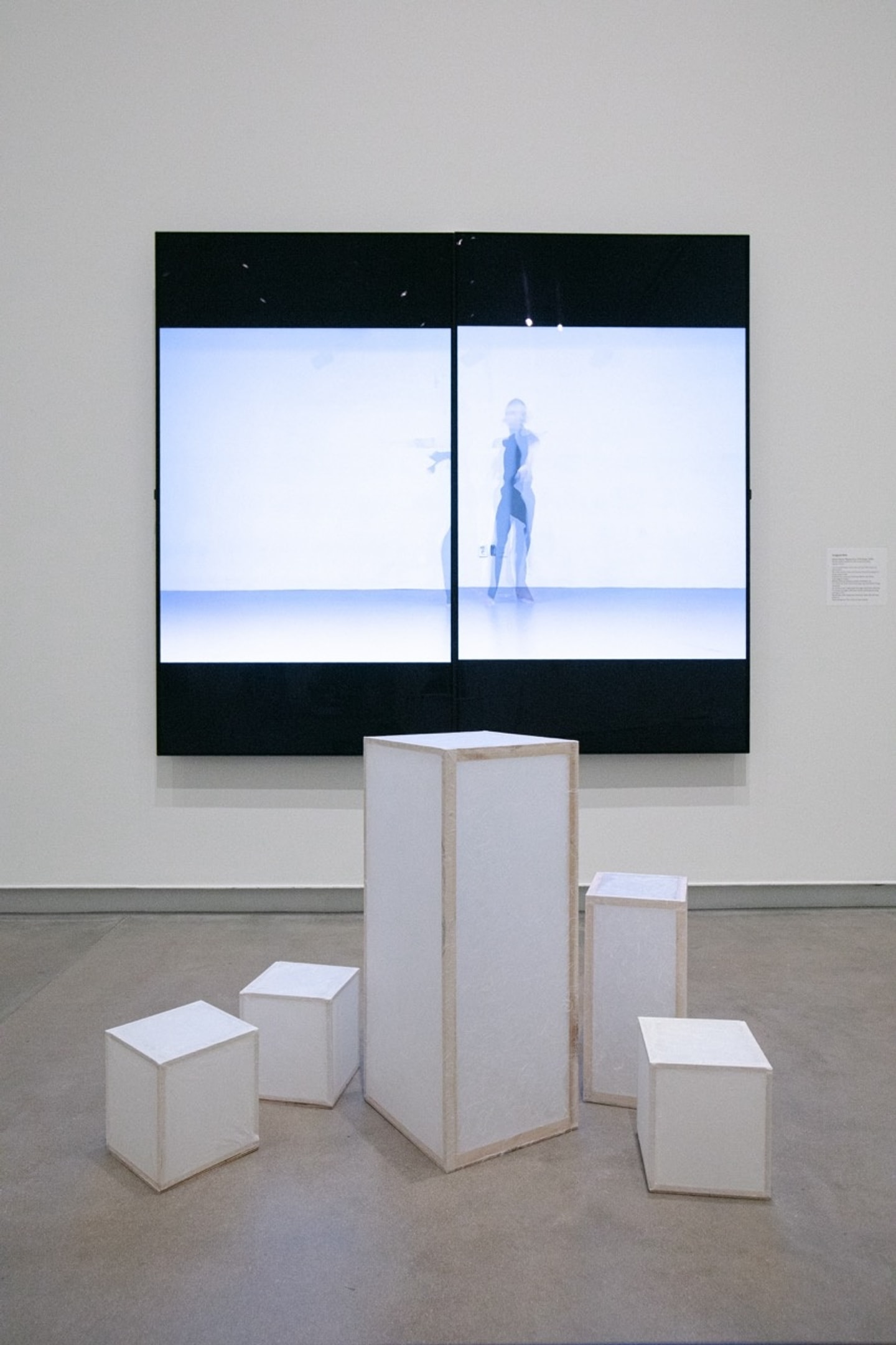 white box sculpture in front of large screen