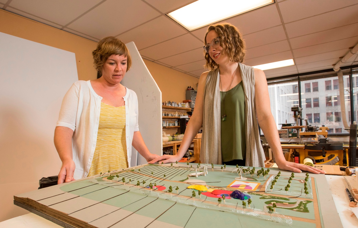 Two people stand on either side of the model of a park, looking at it.