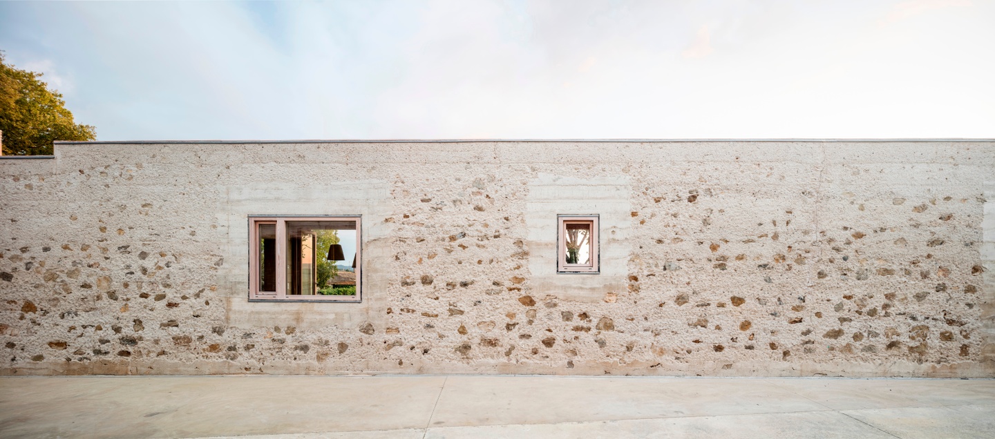 Exterior facade featuring a long, low stone wall with two small window openings looking out into nature.