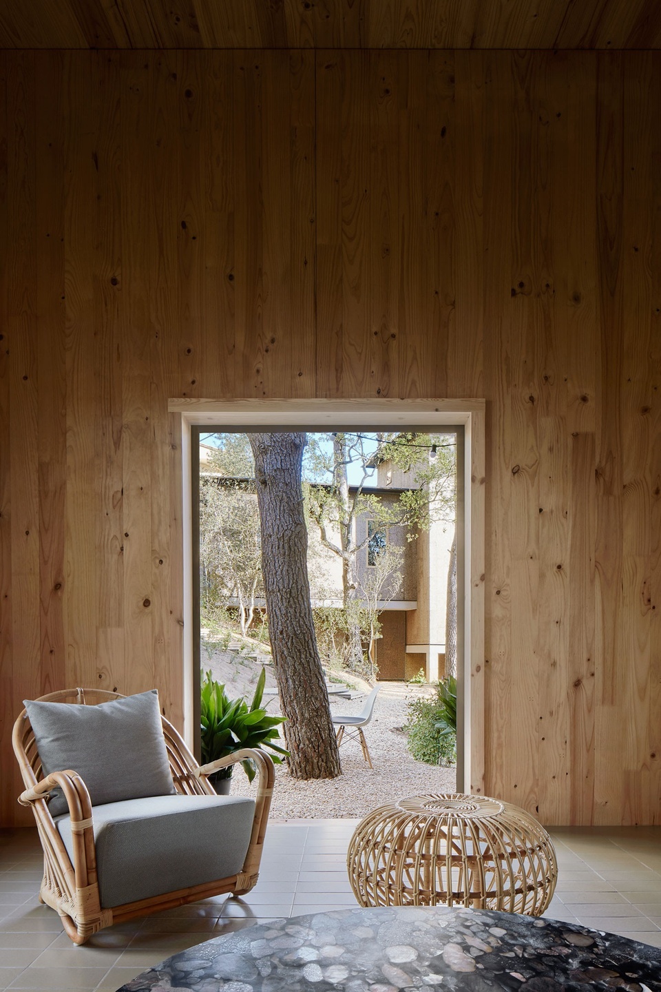 Internal view of the cork house with a cushioned chair and a rattan table. The view outside can be seen through the door opening