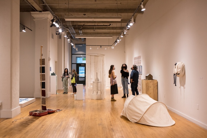 Several people in facemasks stand around a small gallery space looking at artworks and discussing.