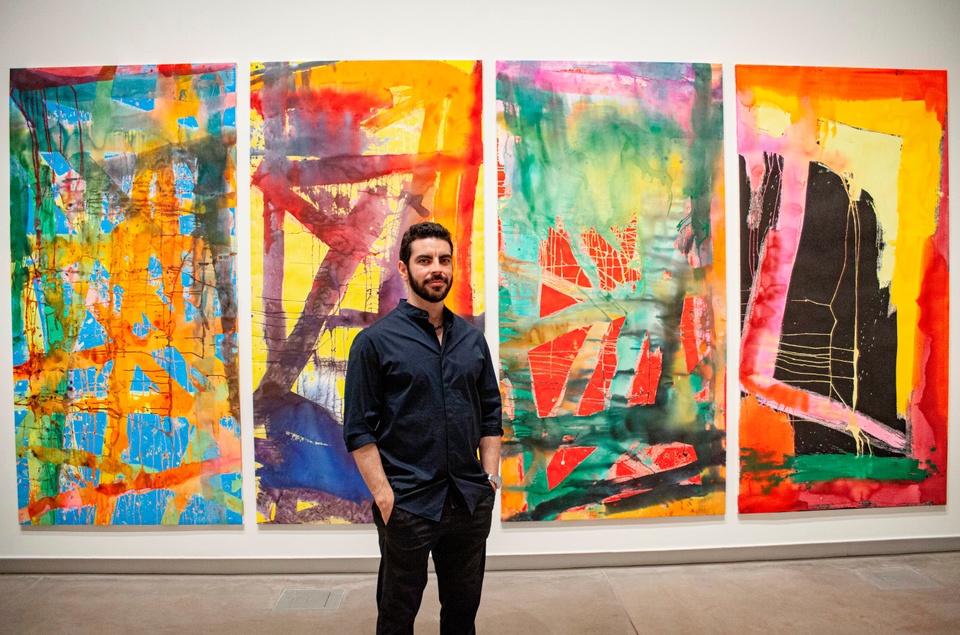 Jorge Rios standing in front of his art of four abstract panels with bright colors