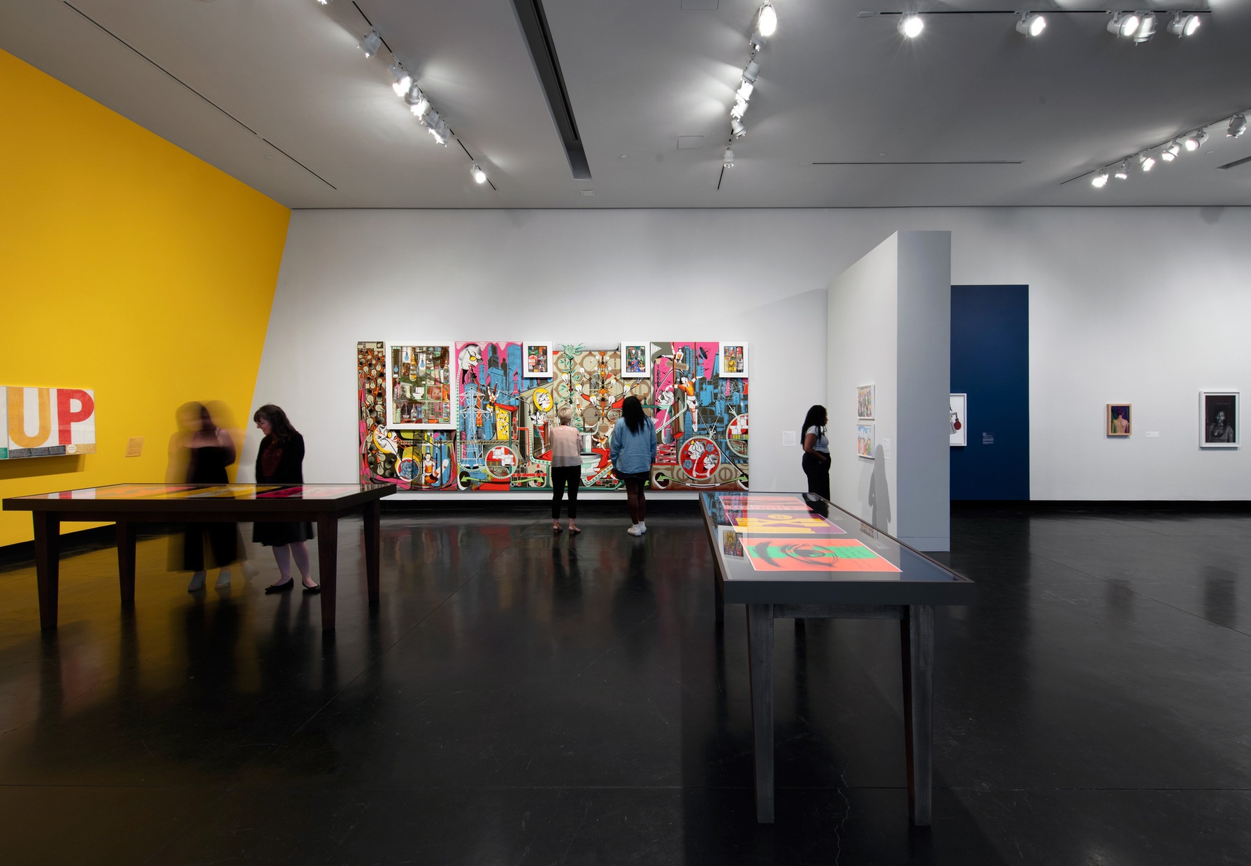 Five people look at artwork throughout a gallery space. A large, colorful abstract painting covers most of one wall.