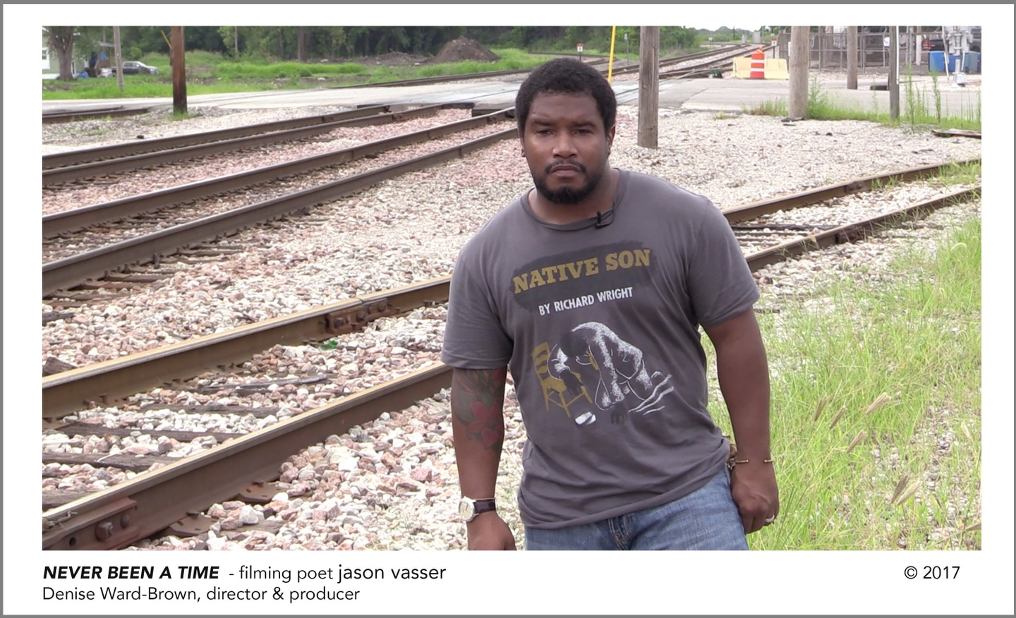 Text reads, "NEVER BEEN A TIME - filming poet jason vasser", below a still from the video, in which vasser stands in front of railroad tracks, wearing a graphic tee that reads, "NATIVE SON BY RICHARD WRIGHT".
