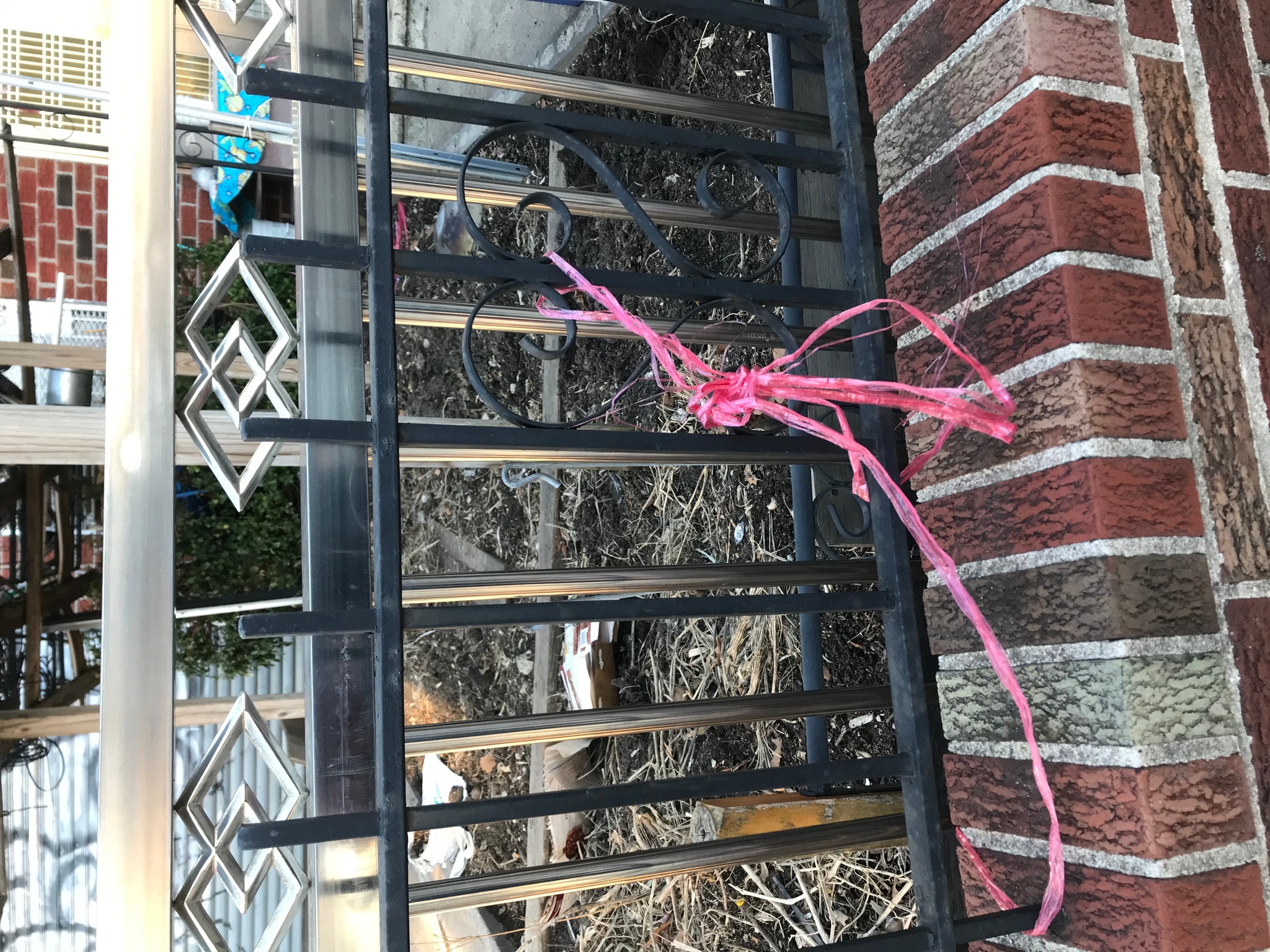 A black wrought iron railing with a stainless steel railing behind it. A piece of pink plastic ribbon is haphazardly tied to the black railing. 