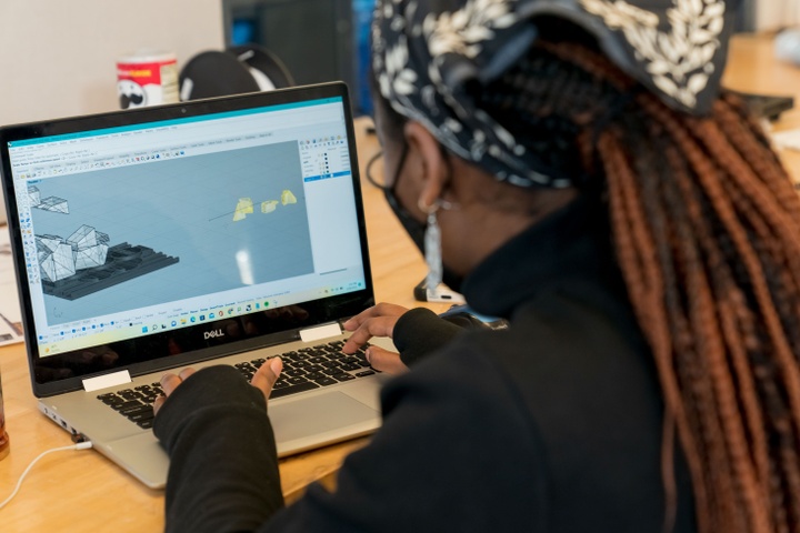 A student whose back is to the camera, working at a computer with an architectural rendering pulled up on screen.