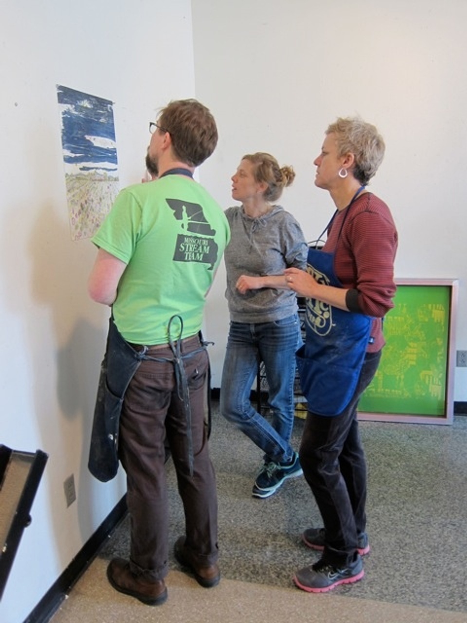 3 people looking at first proof of artist's project on the wall